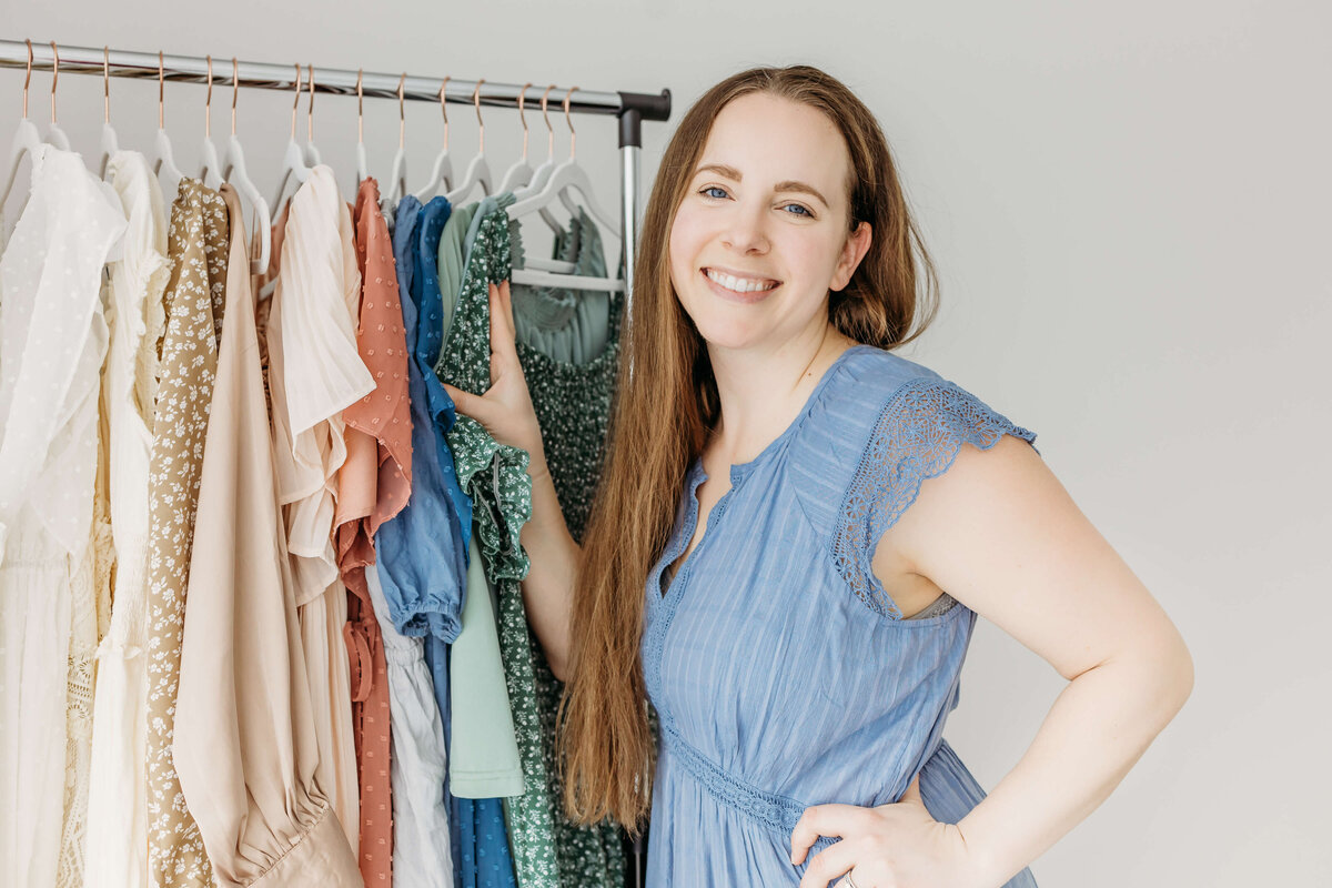 Happy woman in blue dress standing in front of wardrobe rack