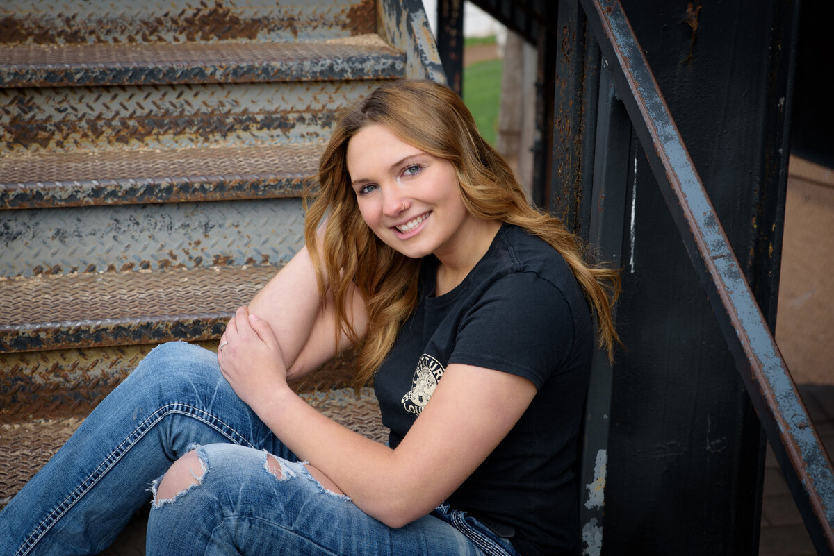 Senior Girl wearing black t-shirt sitting on metal stairs at 141 Raceway in Green Bay, WI