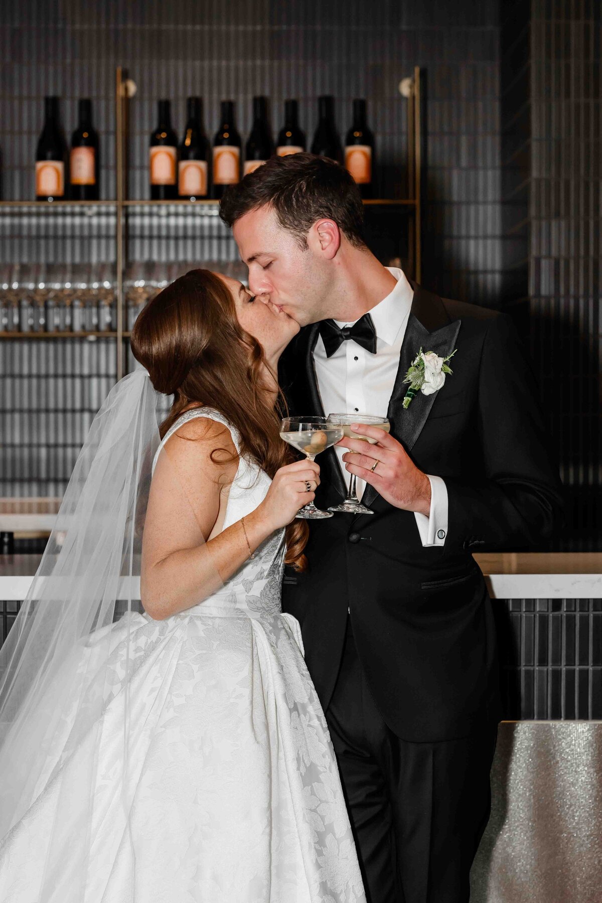 Bride and groom kiss holding cocktails 