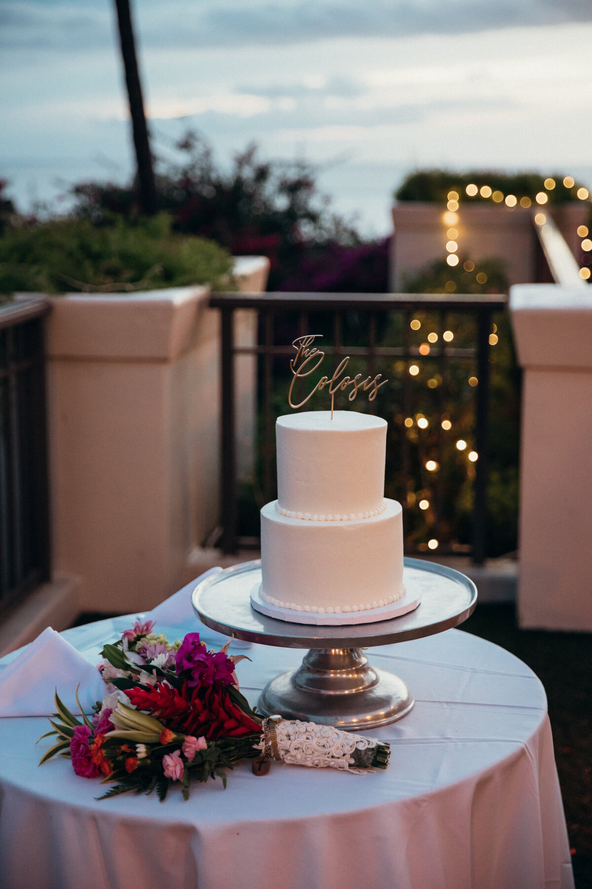 Maui Wedding Photographer captures three tiered wedding cake with bridal bouquet sitting on table