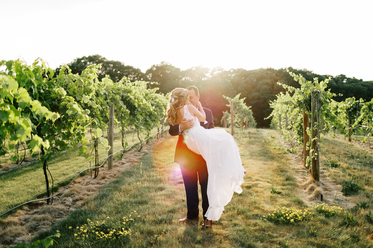 Groom holding the bride in his arm under the sun setting sun