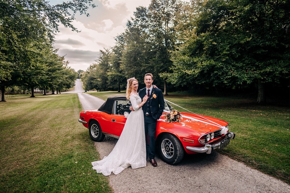 Bride and groom in front of red car