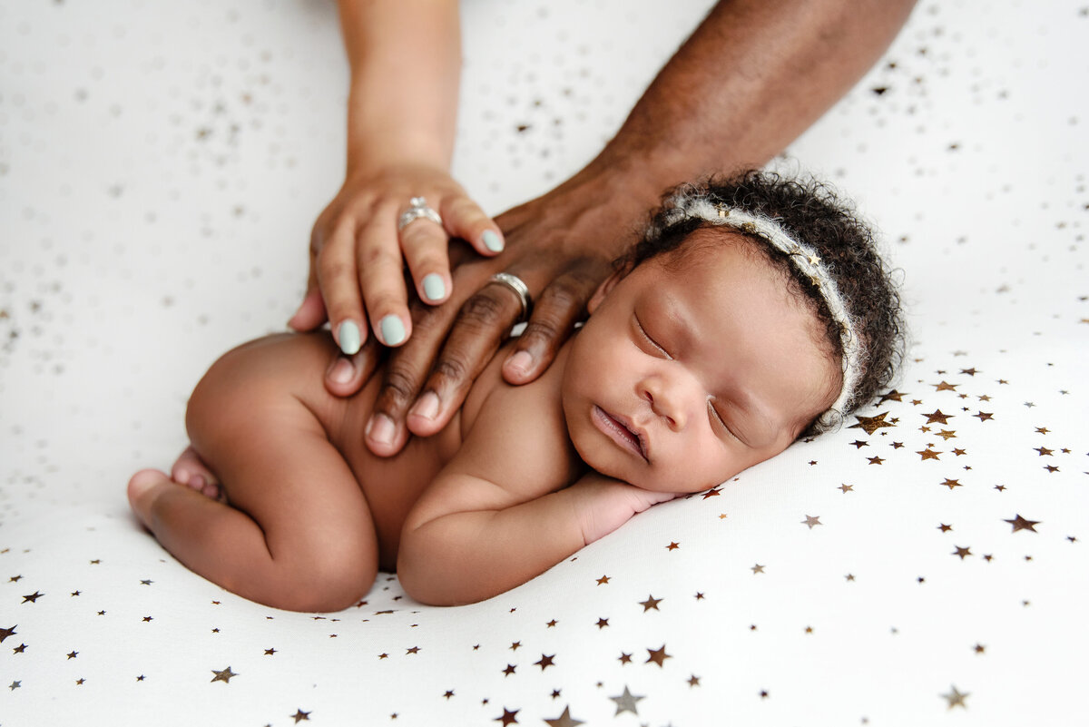 st-louis-newborn-photographer-sleeping-baby-on-white-starry-blanket-while-mom-and-dad-place-hands-over-child