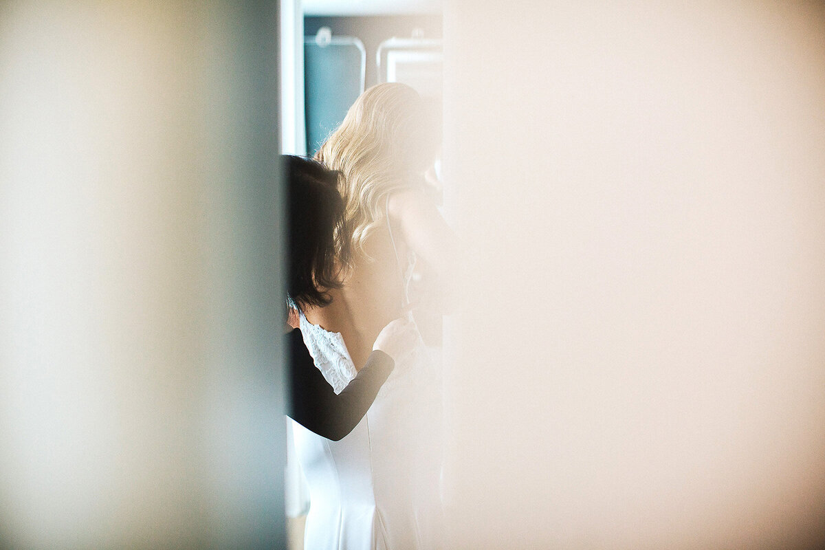 Bride seen through crack in door getting dressed.