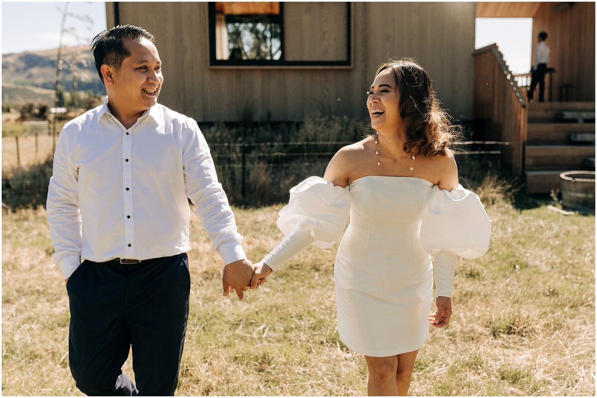 couple wedding day holding hands laughing short white cocktail dress with puff sleeves christchurch five acre farm photographer white shirt cabin