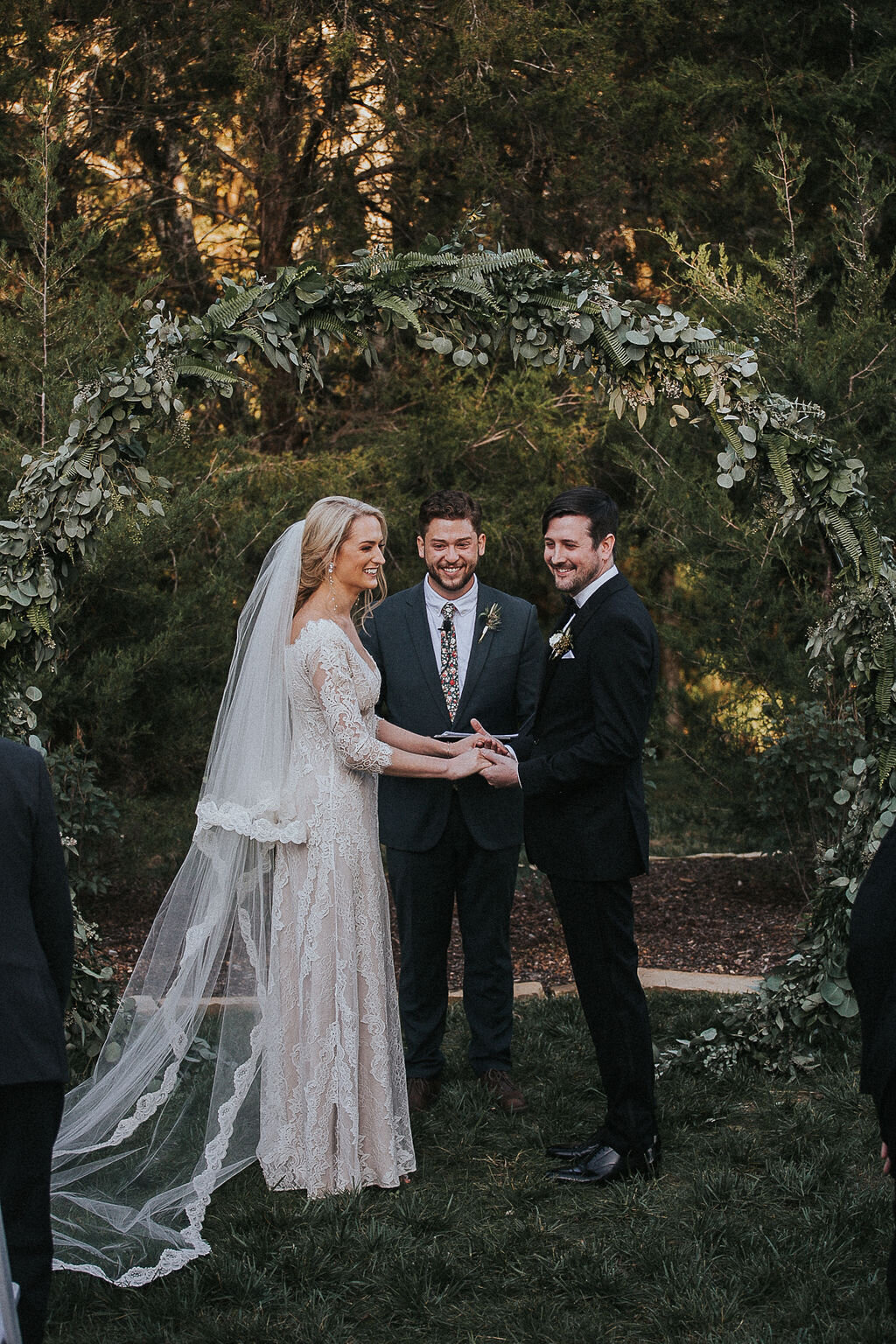 Bride and groom standing in front of a circle arbor covered in greenery