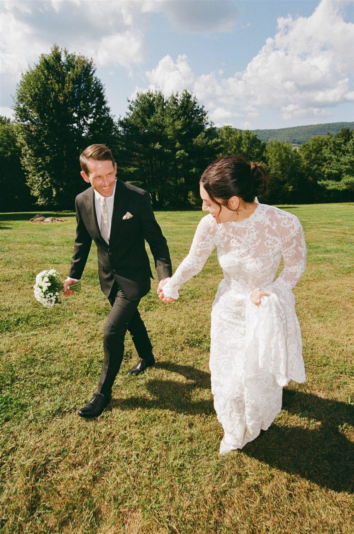 groom-holding-bouquet-laughs-while-walking-with-bride