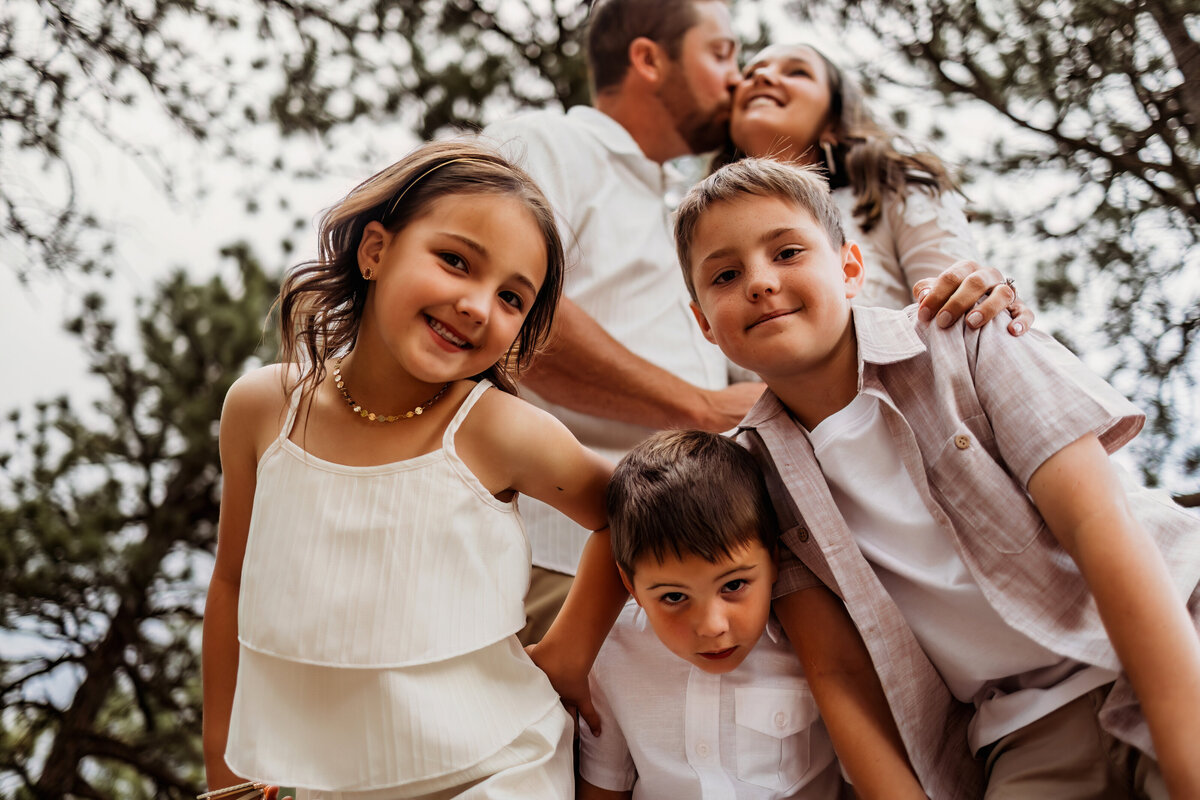 kids being silly and looking down at the camera while mom and dad embrace in the background for their family session in colorado