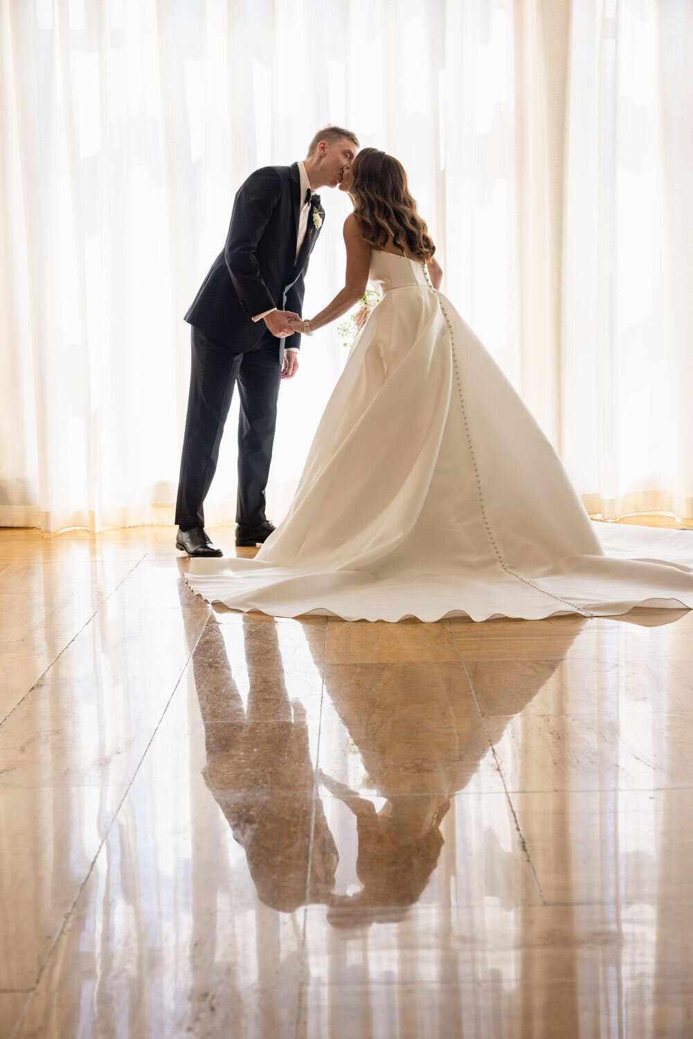 A bride and groom kissing in front of a window