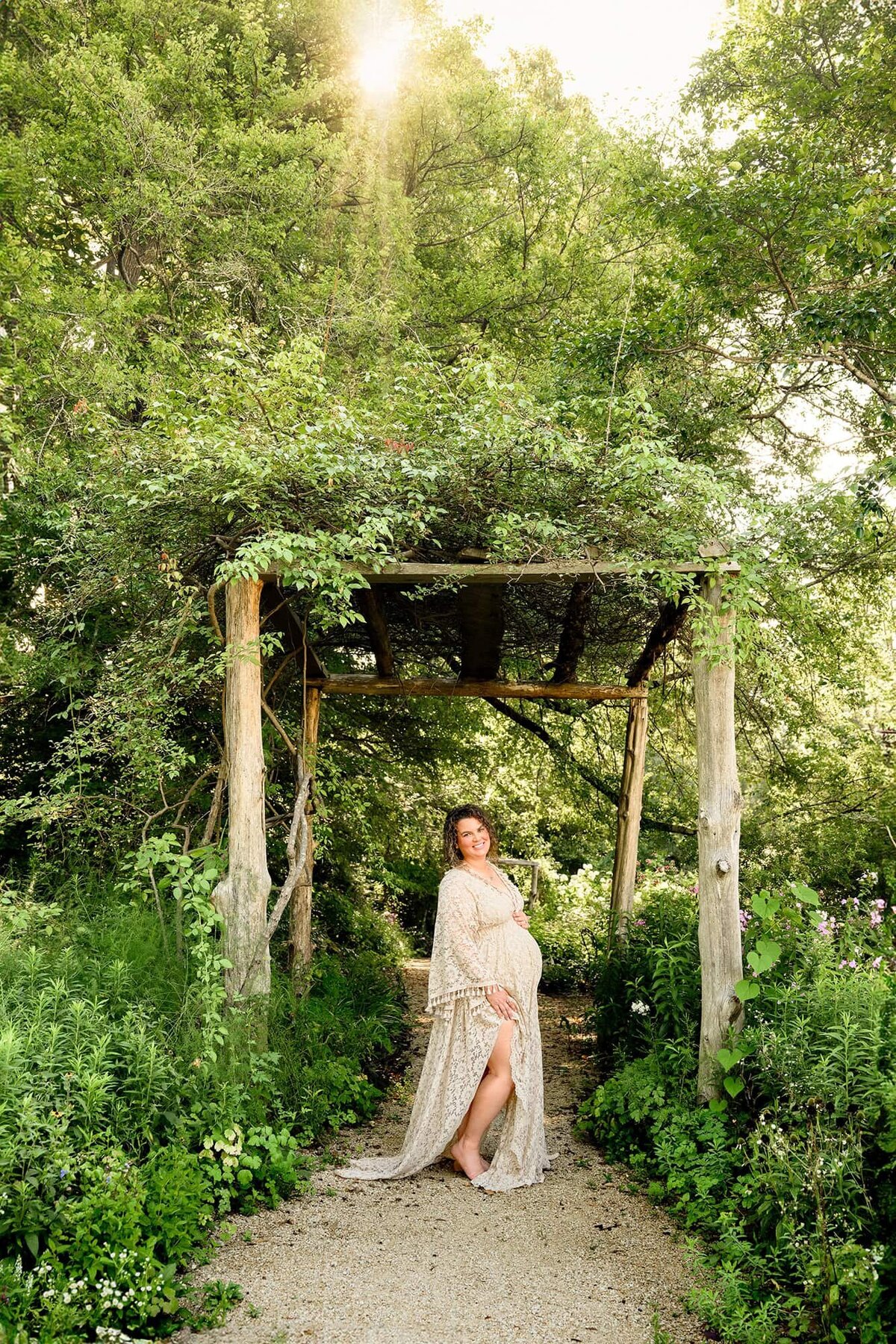 maternity photo of pregnant charlotte mom wearing a cream dress under a natural arbor 