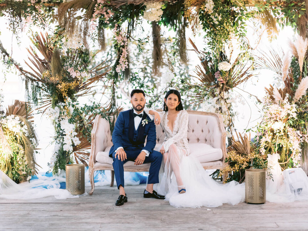 The bride and groom are sitting on an elegant white couple's couch in Khayangan Estate, Indonesia. Image by Jenny Fu Studio