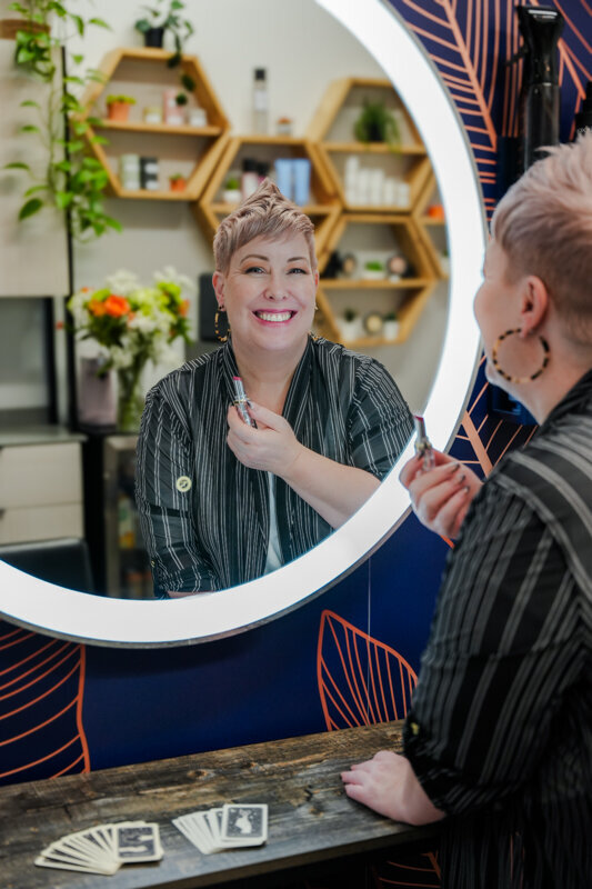 Kirsty Shelley in her salon looking in the mirror and smiling while applying lipstick
