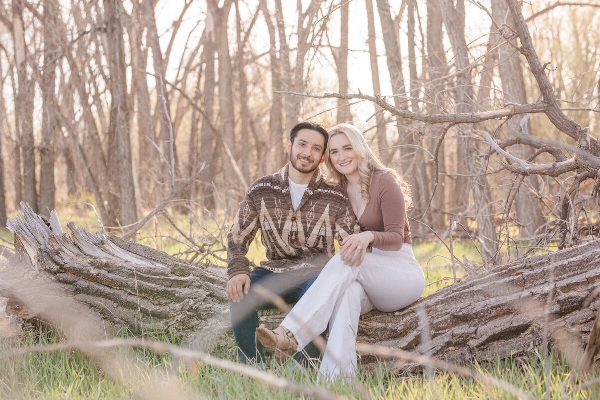 A newly engaged couple smiles for the camera while seated on a fallen cottonwood tree near Boulder, Colorado