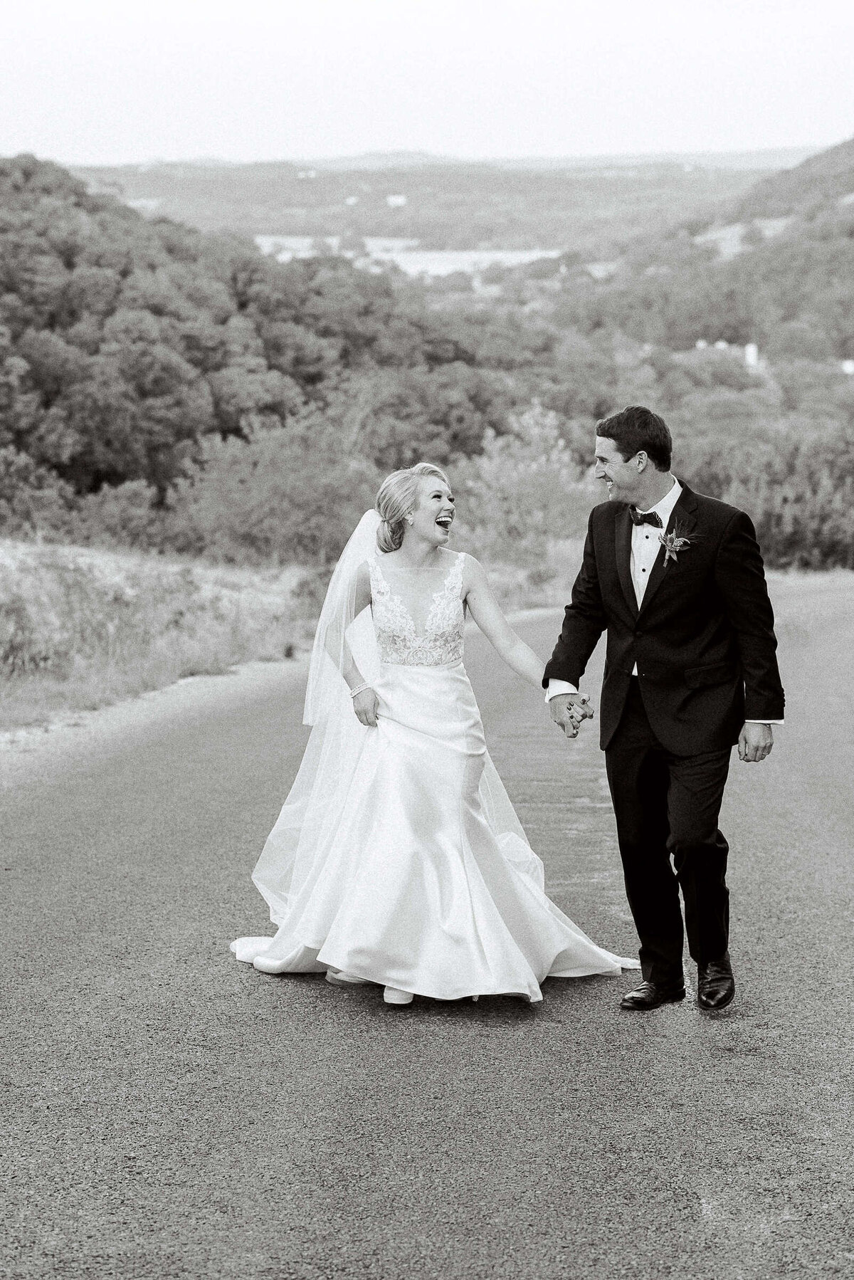 Joyful bride and groom run through Texas hill country while holding hands and laughing