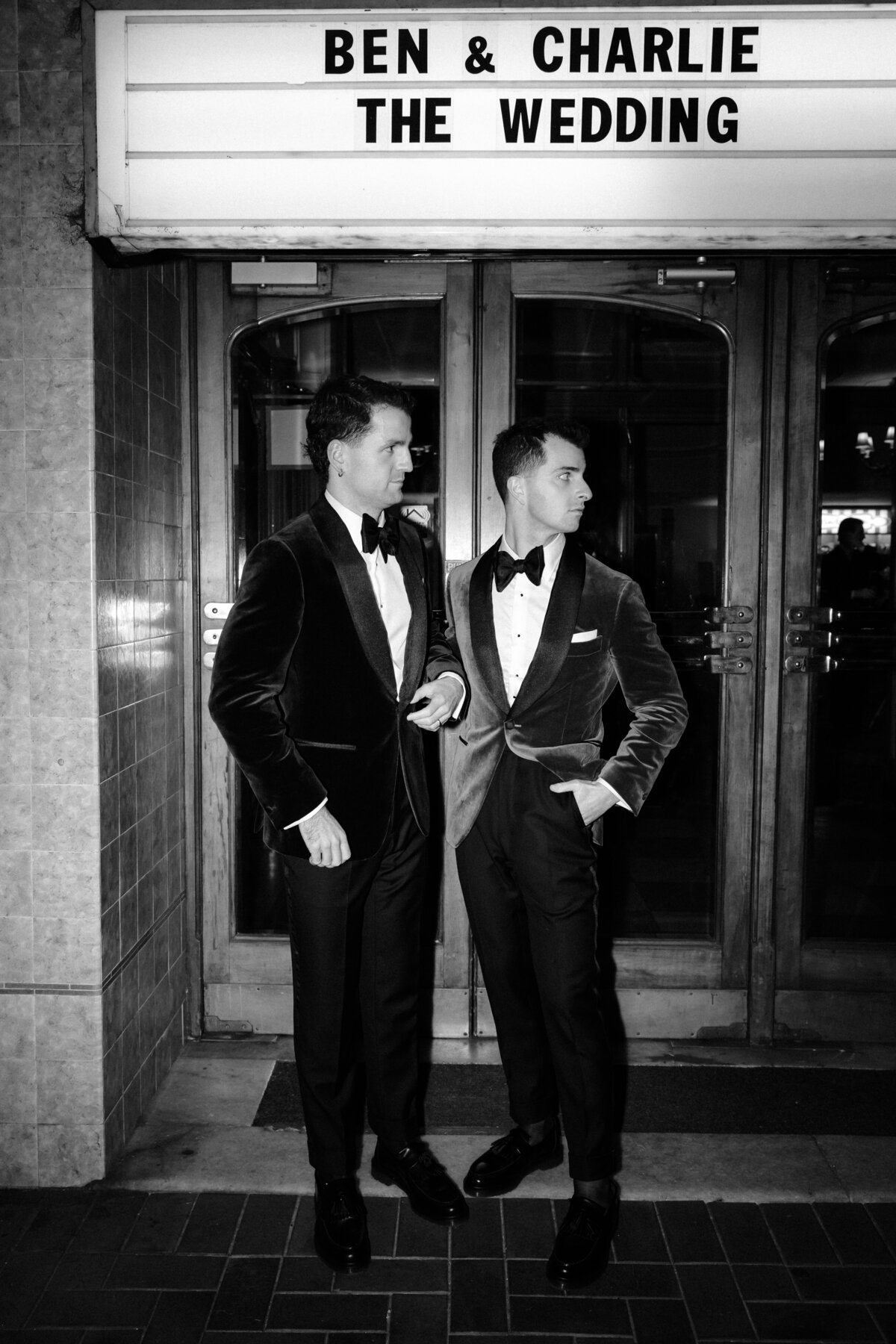 2 grooms looking at the side, outside their regal cinema wedding.