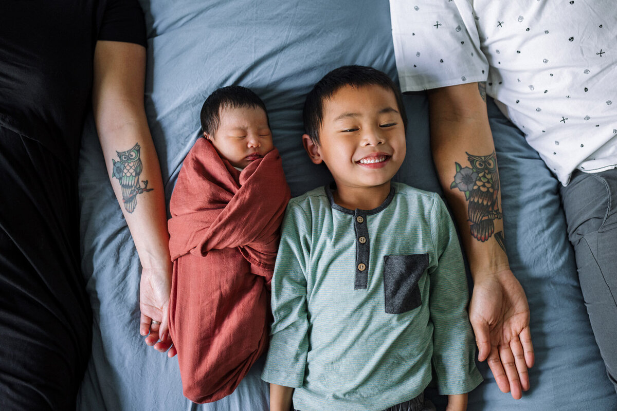 5-year-old boy laying next to swaddled newborn sister between parents with matching owl tattoos