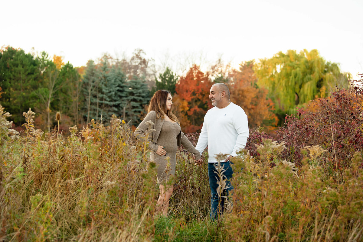 husband and wife holding hands in a field for their fall maternity photography session in Burlington, Ontario