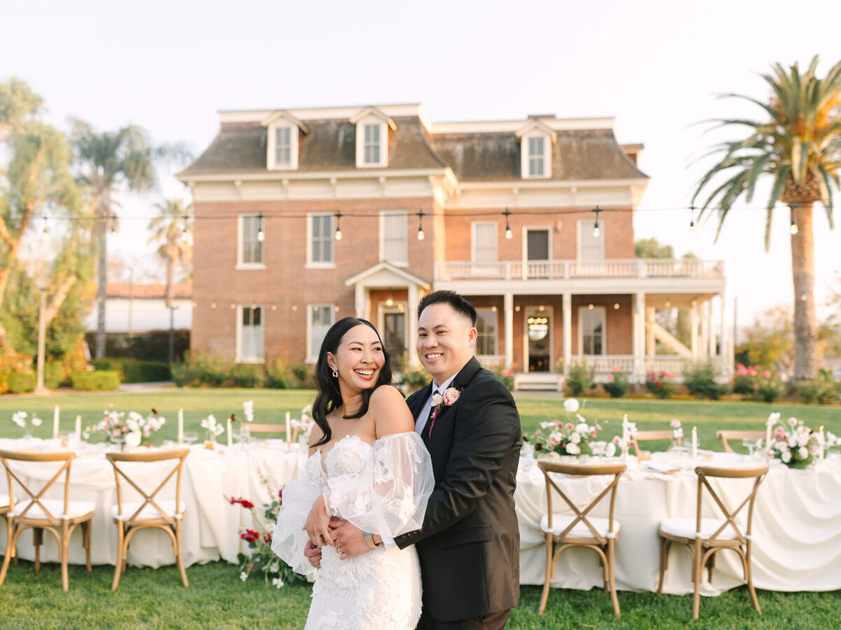 A joyful couple in wedding attire stands in front of the Barton House of Redlands.