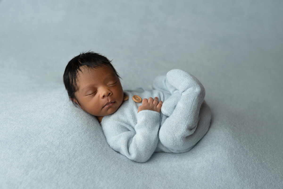 A newborn baby sleeps on its back in a onesie with buttons in a New Orleans Newborn Photography studio