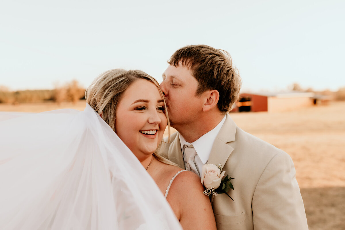 groom kisses the brides forehead as she laughs and looks back to him in their outdoor wedding captured by Best Little Rock wedding photographer