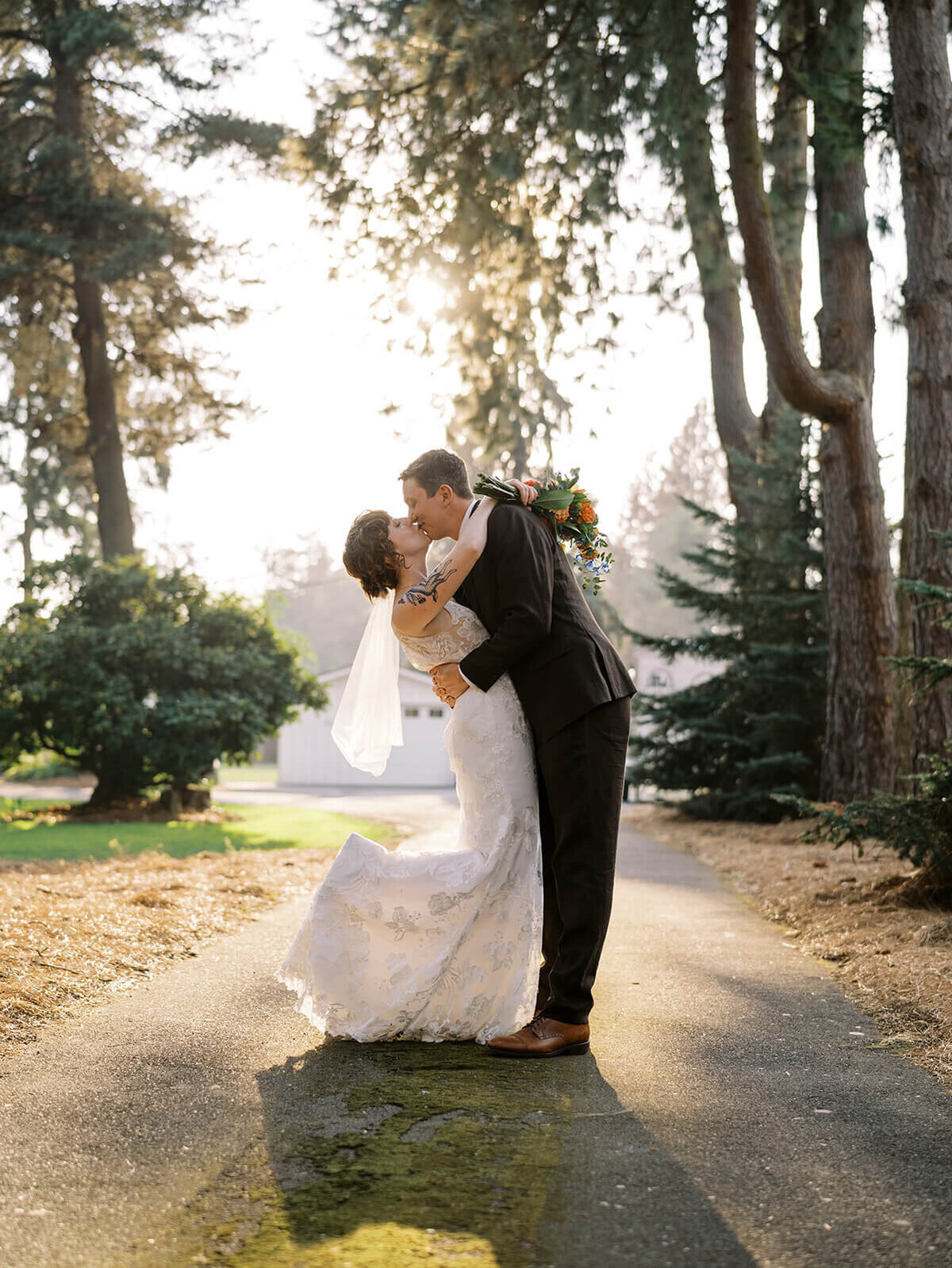 Bride and groom kissing in a road with sunlight behind them. 