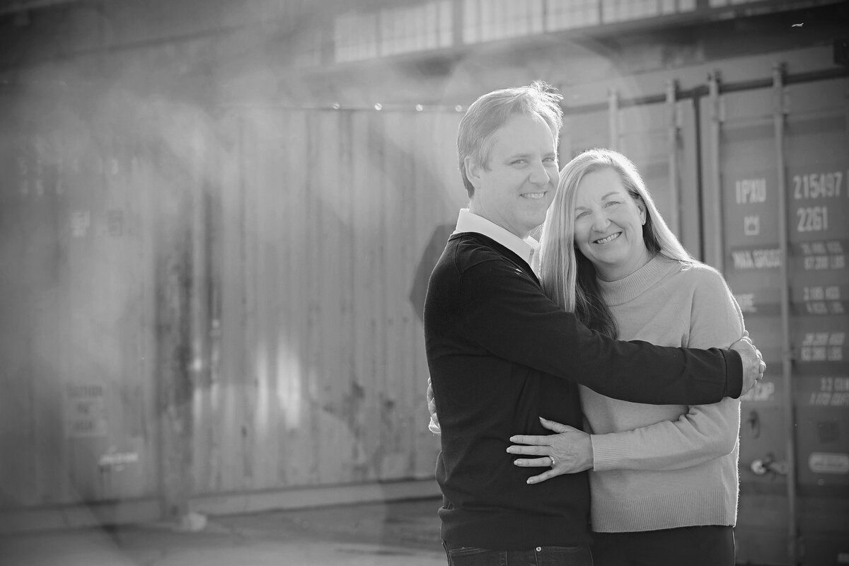Black and white portrait of smiling couple standing together in front of orange metallic van at Camp North End Charlotte NC