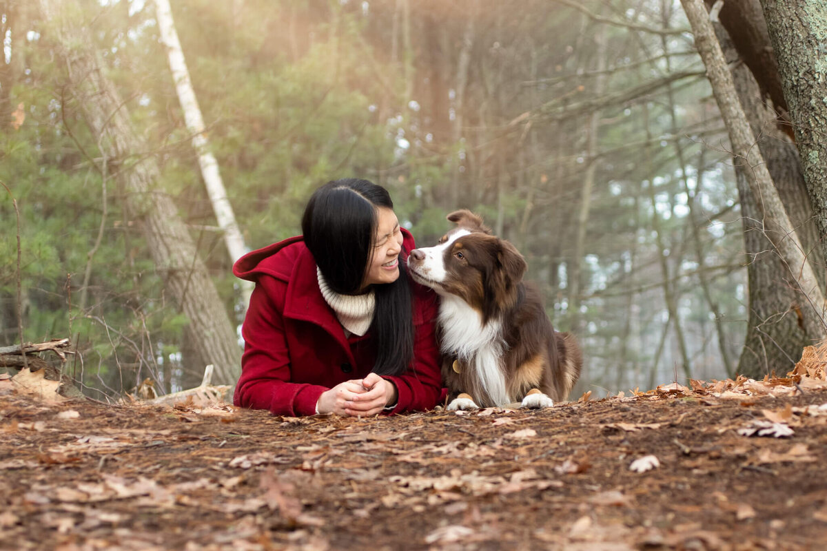 Dog Mom in red pea coat getting a kiss from her dog in the Boston area Reading woods