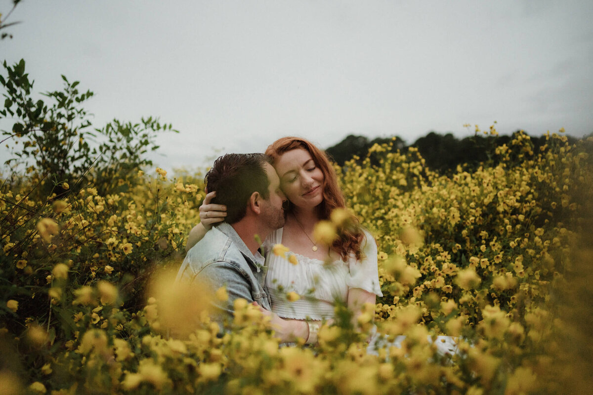 couple cuddling in a field of yellow flowers