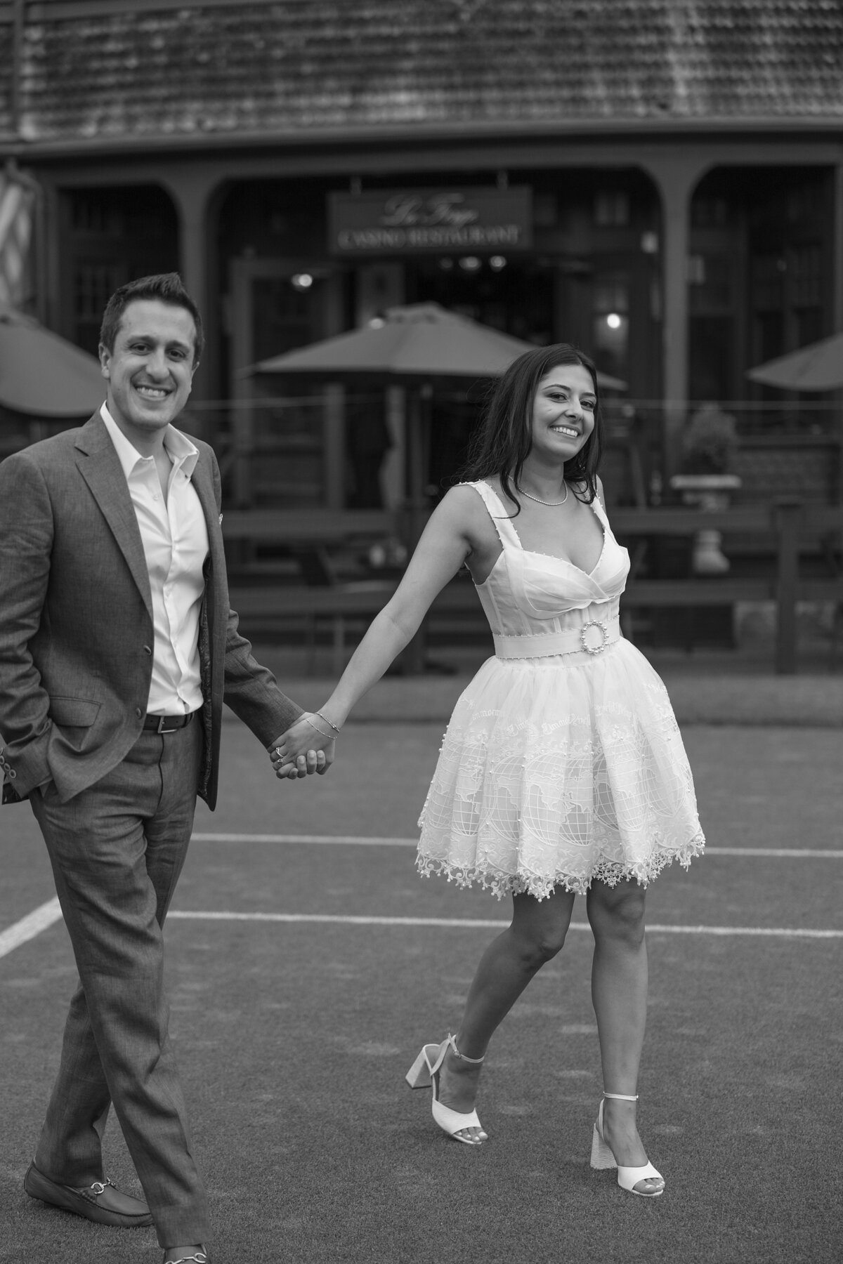 Couple smile at camera as they walk across the lawn of the Tennis Hall of Fame in Newport, Rhode Island.