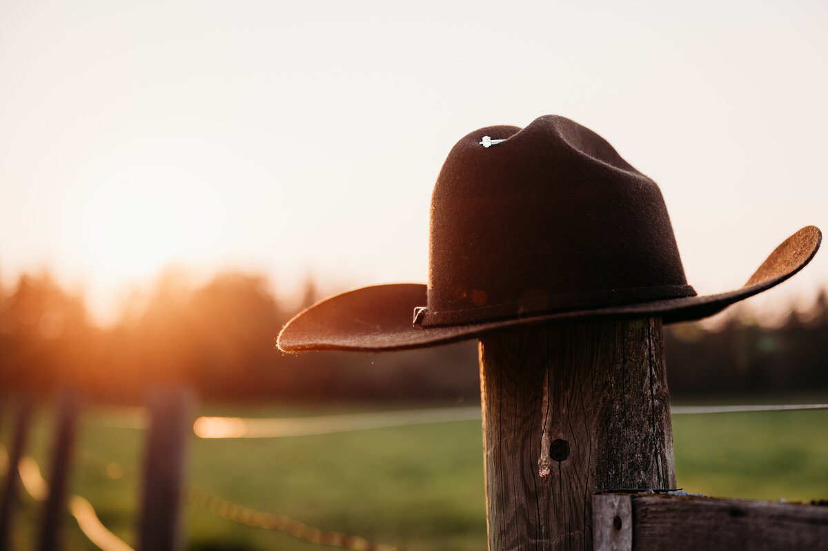 cowboy hat sitting on a fence post holding a brides ring, golden sun shining in the background