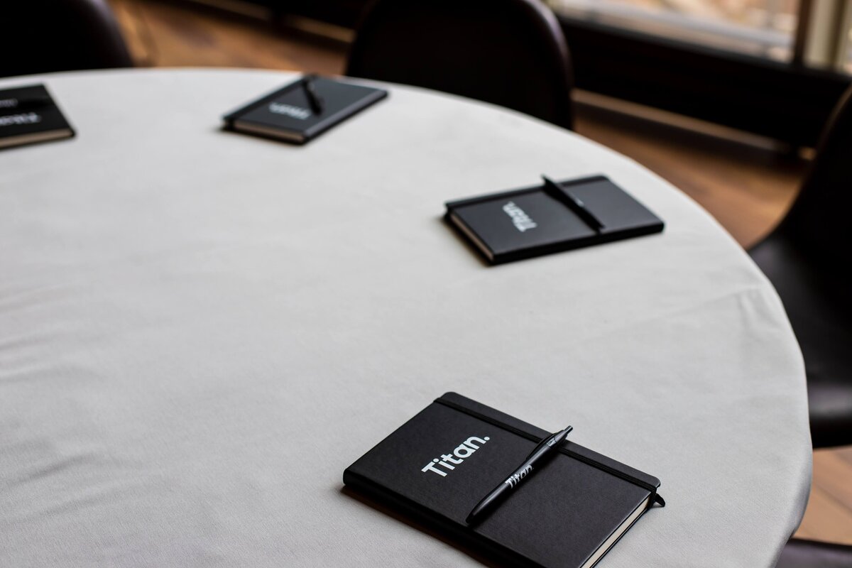 Close-up of Titan-branded black notebooks placed on a round white table.