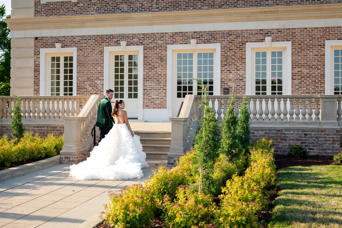 Discover the timeless beauty of a wedding at a historic mansion. This stunning bridal photo captures a couple ascending elegant stone steps, surrounded by lush greenery and classic architecture. Perfect inspiration for your dream wedding venue.