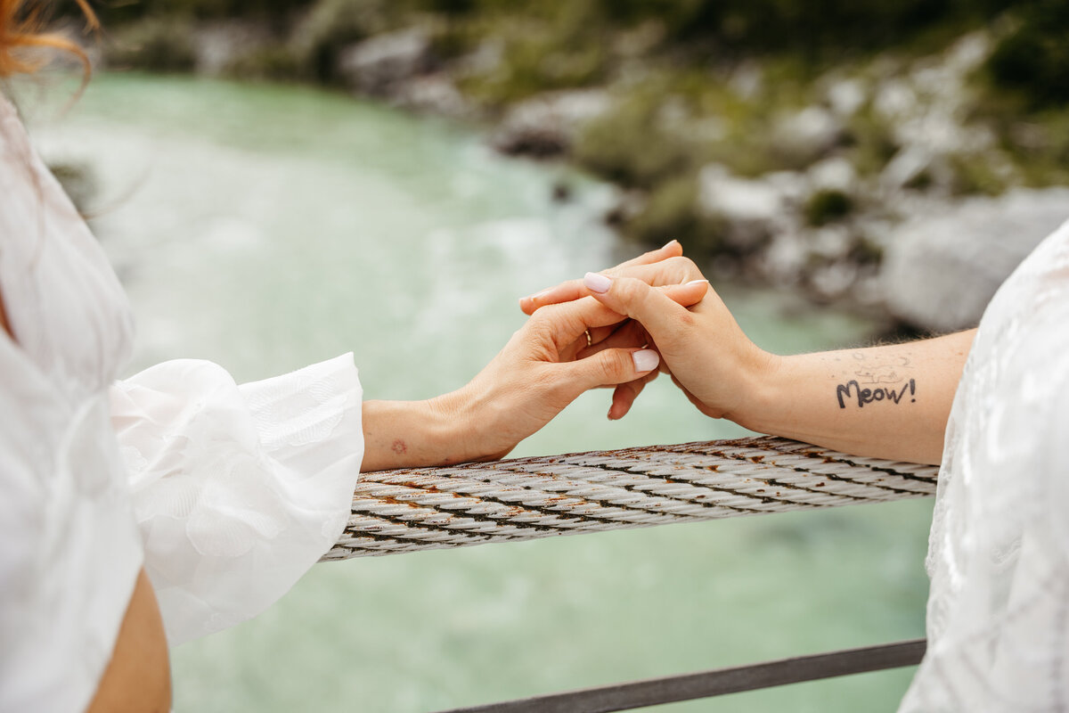 Brides holding hands on suspension bridge Soča Valley