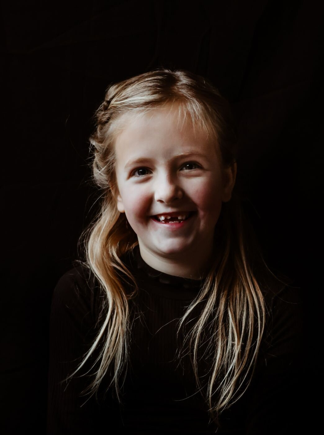 Een portretfoto van een jong meisje met een stralende glimlach, gefotografeerd tegen een donkere achtergrond
