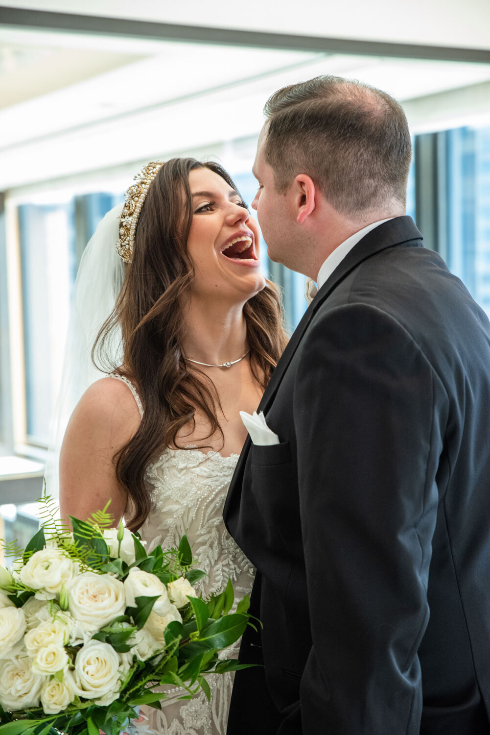 A bride and groom are laughing together and the bride is wearing a tiara