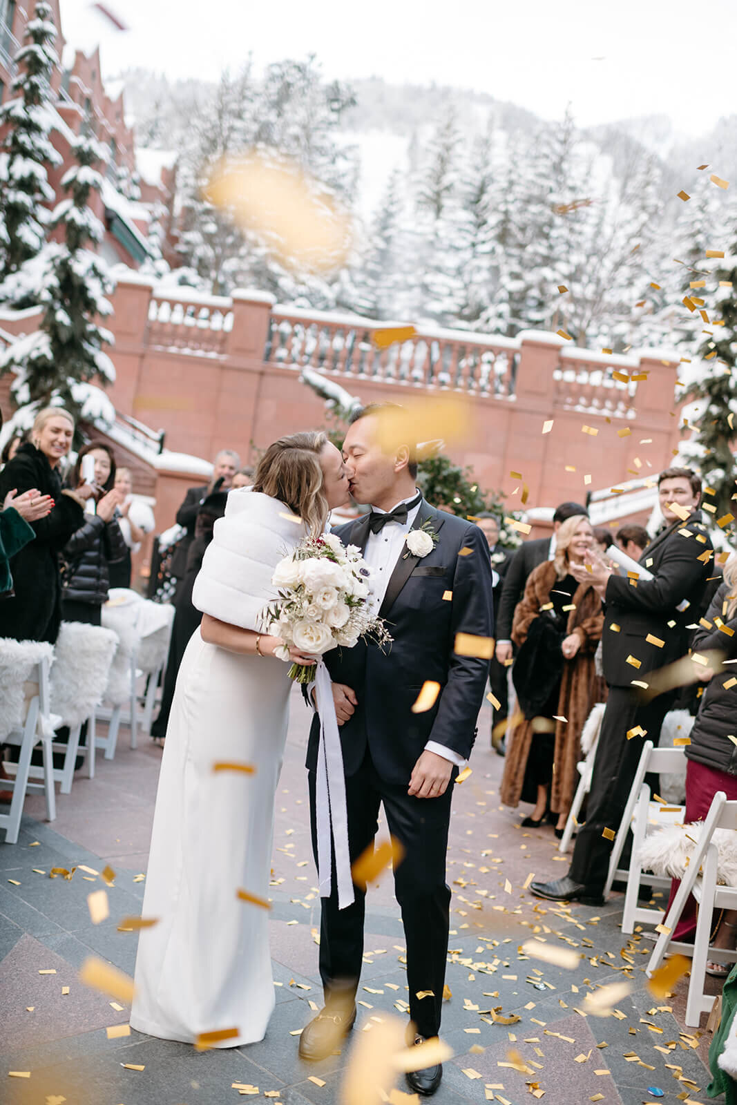 Bride and groom sharing a kiss during their wedding processional at St. Regis Aspen, surrounded by guests and confetti.