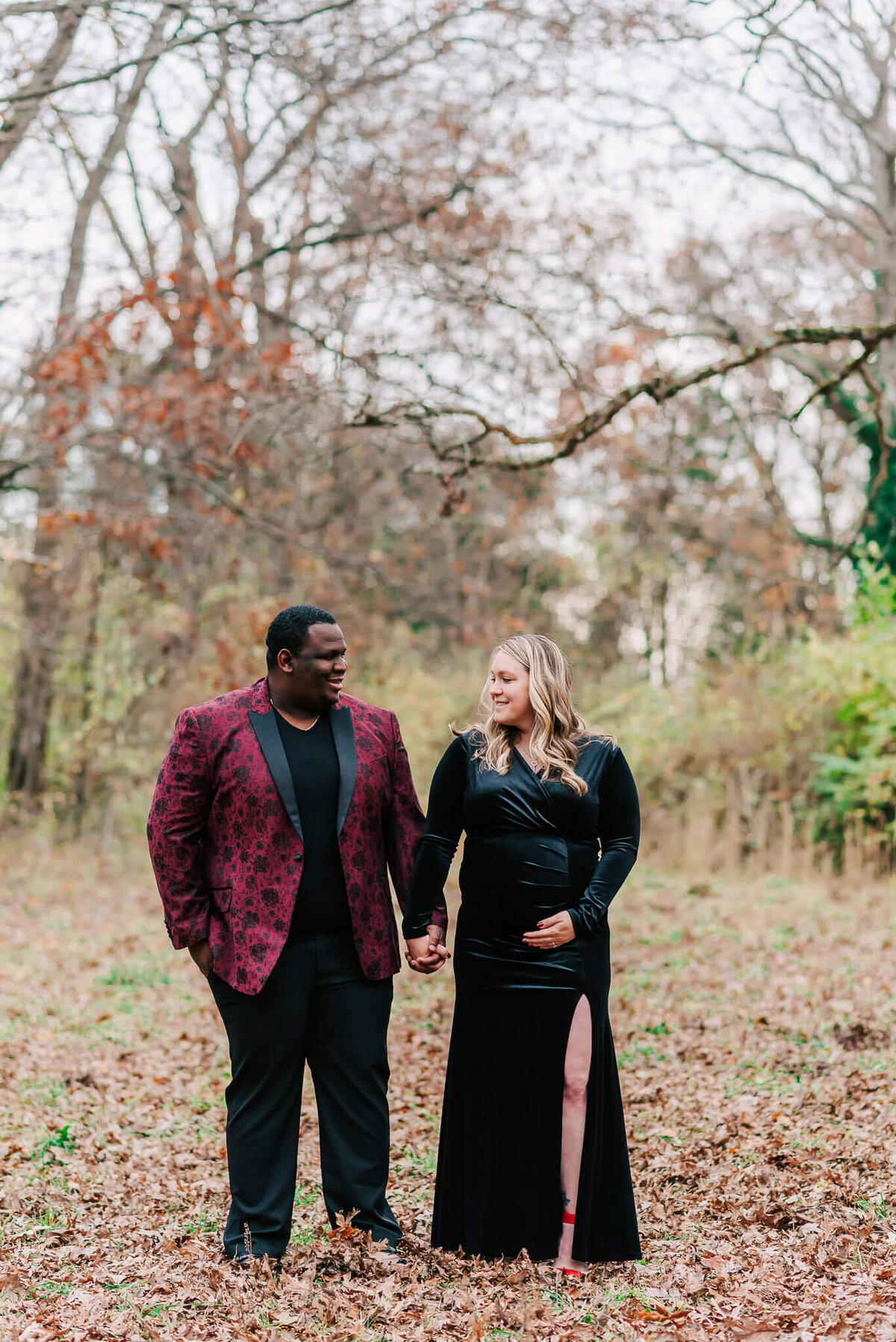 A man in burgundy holding hands with a pregnant woman in black velvet