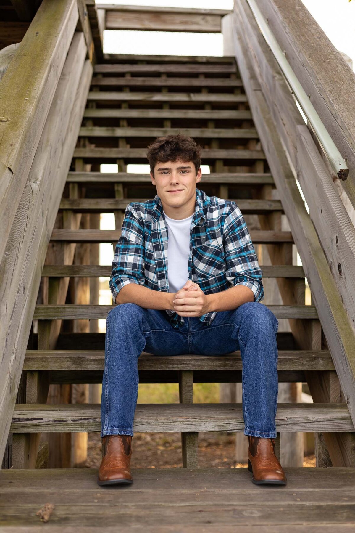 A senior guy sitting on wooden stairs leaning on his knees in Lawrence KS