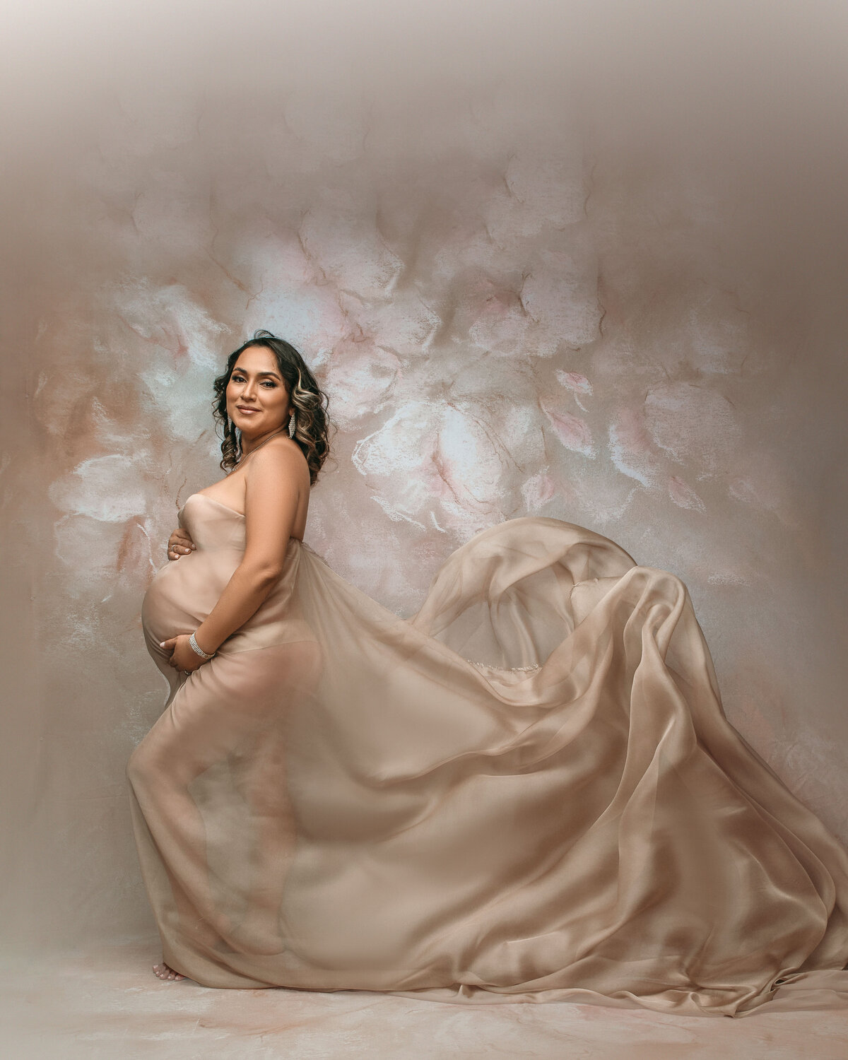 34 weeks pregnant woman posing in portrait studio wearing cream chiffon fabric flowing behind her