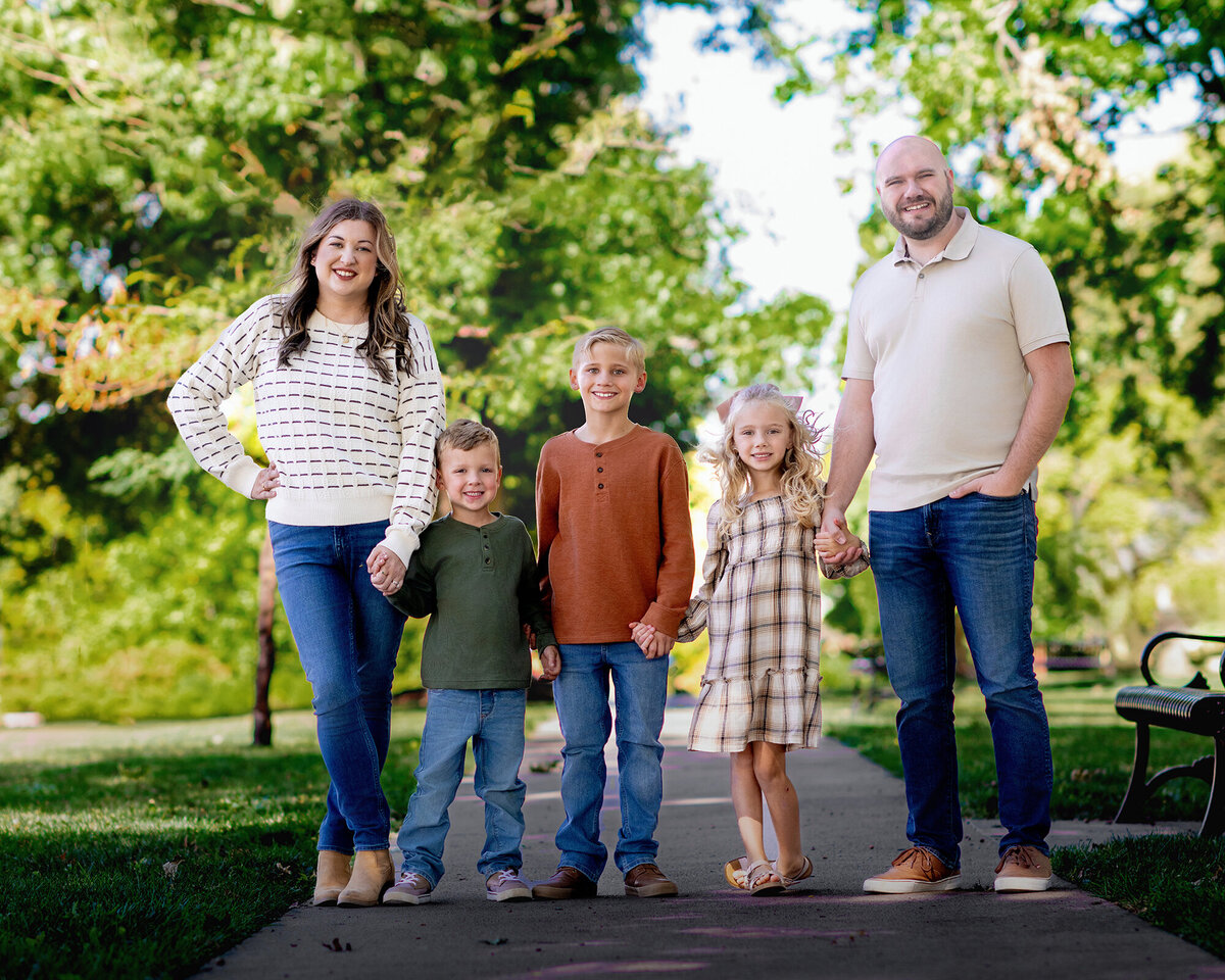 Family of 5 standing together in a lush green garden with plants and flowers surrounding them.