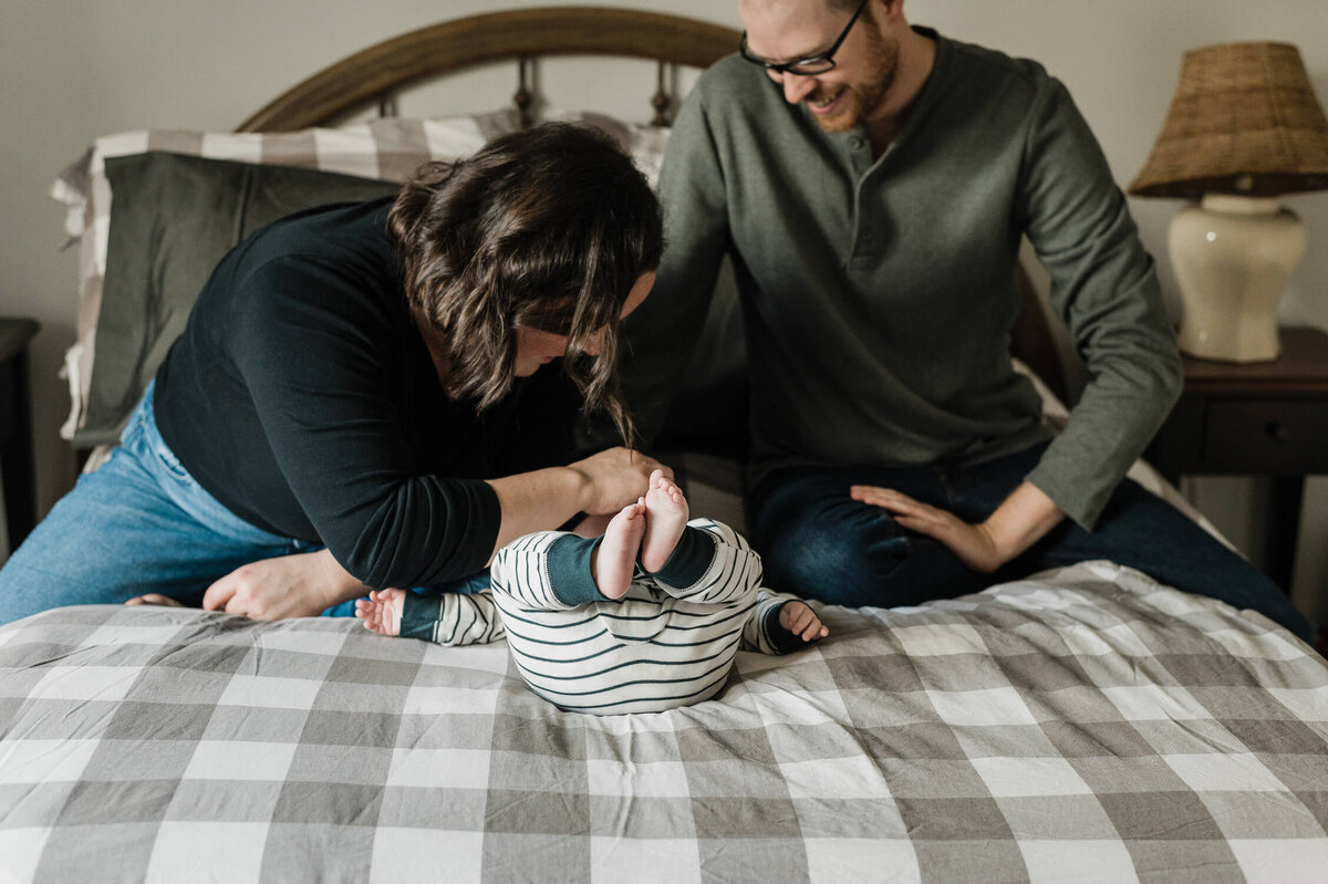 Couple playing with baby on plaid bedspread.