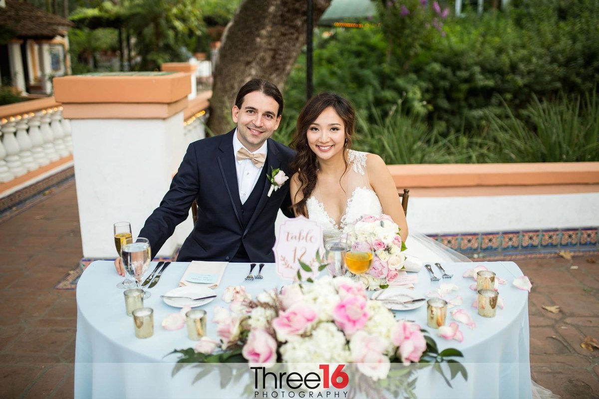 Bride and Groom pose for a photo sitting at the Sweetheart Table