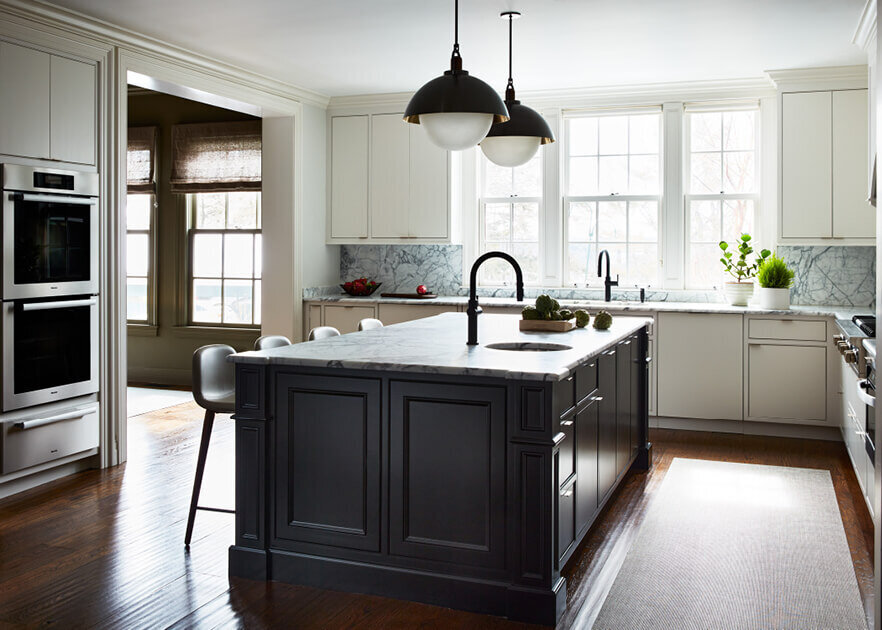 A modern kitchen in a traditional home features a black island and Allied Maker pendants, blending classic architecture with bold, contemporary design.