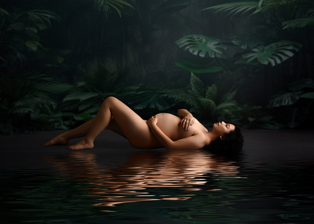 expecting mom surrounded by green tropical plants laying down nude with water reflection, beautiful studio light in my Arizona Maternity studio