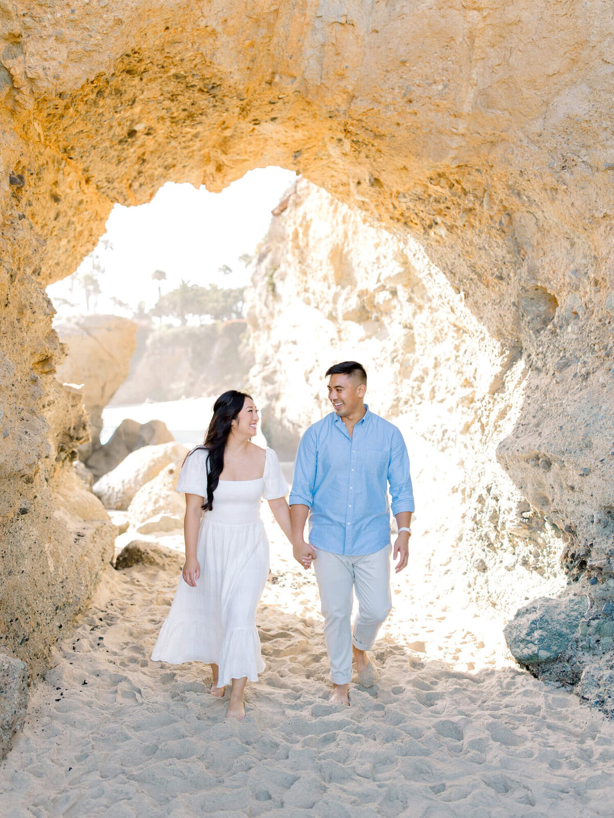 couple engagement photo walking underneath cliff arch