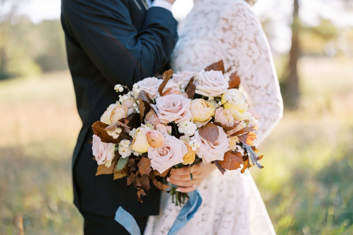 Image of a couple standing in wedding attire facing each other with the bride holding a big bouquet of fall blooms.