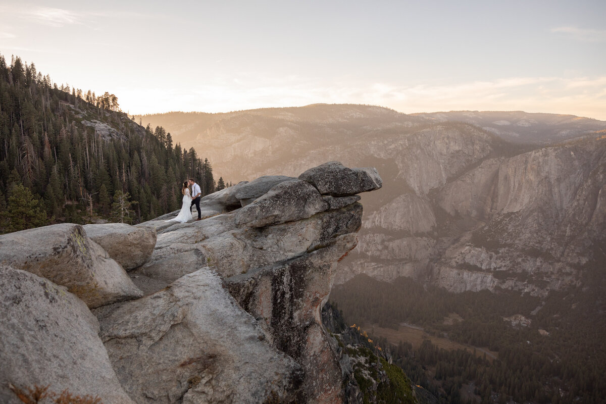 A bride and groom kiss while standing on the edge of a cliff on their elopement day in California,
