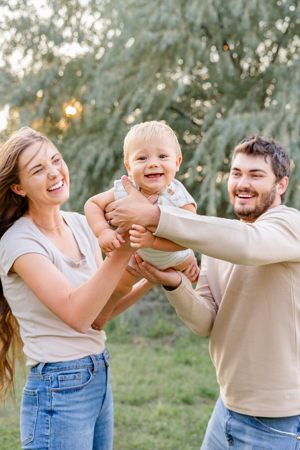 A bright-eyed baby laughing while being lifted by loving parents, radiating happiness.