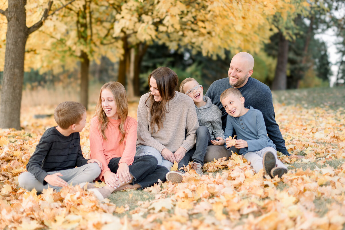 family cuddling together on the ground surrounded by fall leaves