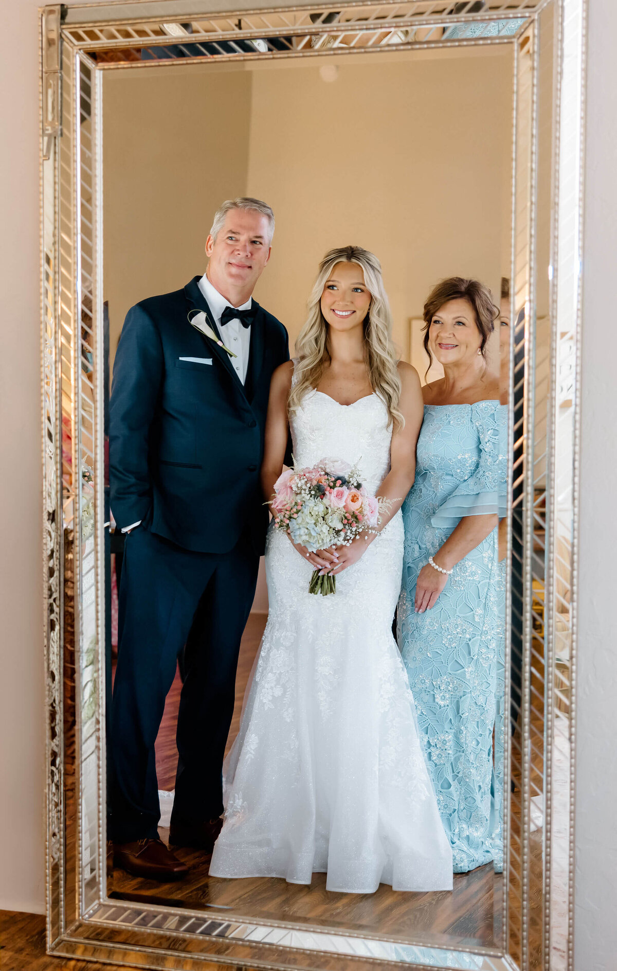 parents of bride looking at bride in mirror in bridal suite before wedding day ceremony